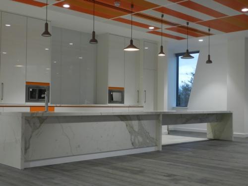 orange ceiling cladding above white marble kitchen with orange accents